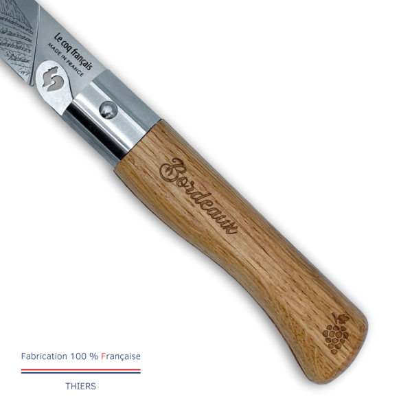 Gros plan manche chêne français verni du couteau de poche pliant Le Coq Authentique Bordeaux, gravure laser Bordeaux en belle typographie et fine grappe de raisin